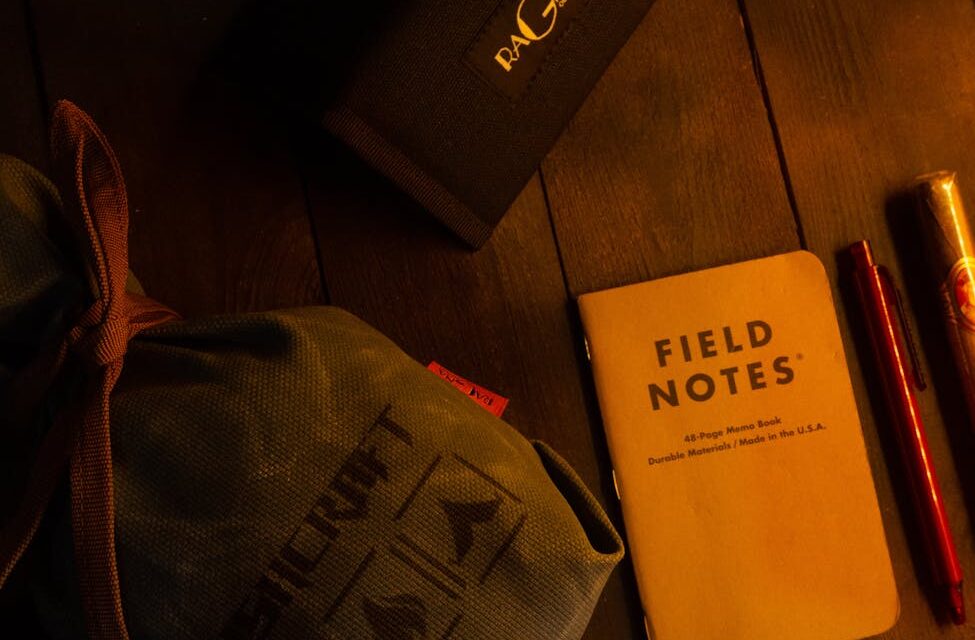 top view of a notebook with pens and bags lying on a wooden floor